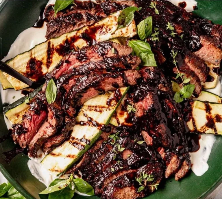Marinated balsamic flank steak served on a plate with herbs and vegetables