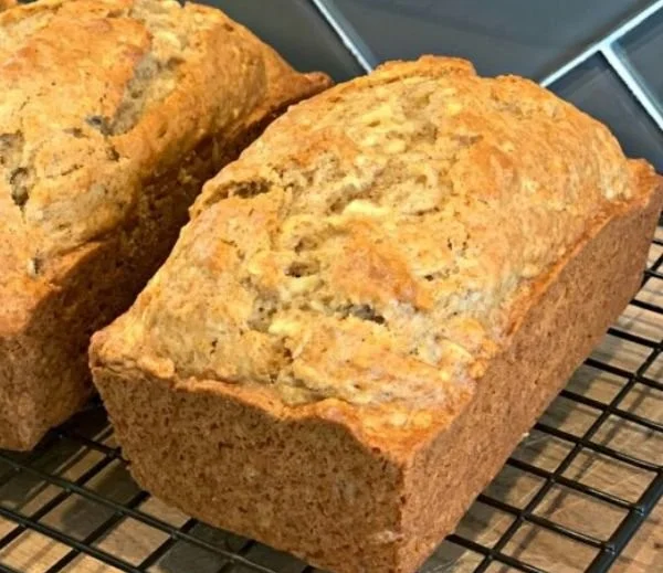 A slice of homemade apple bread with chunks of apples and spices on a wooden table.