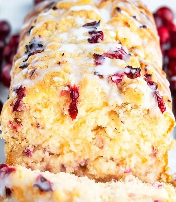 Delicious cranberry bread topped with orange glaze on a wooden table.