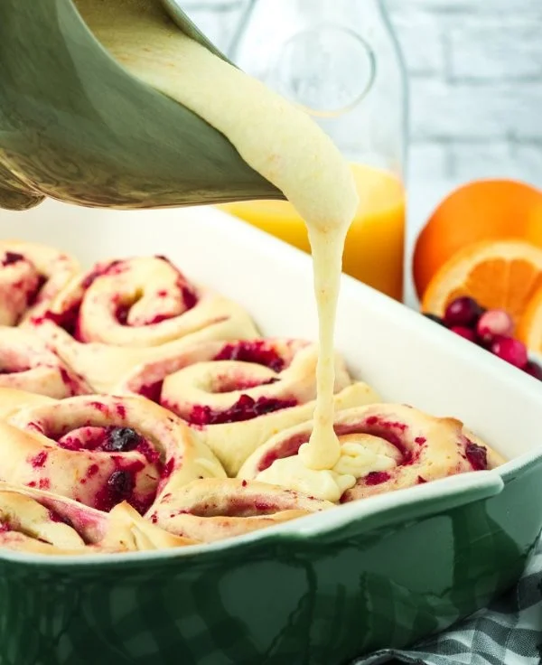Cranberry orange sweet rolls drizzled with icing on a white plate.