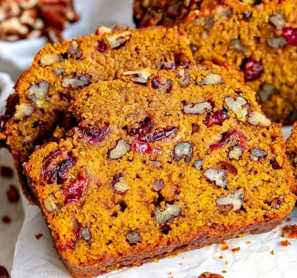 Sliced cranberry pecan pumpkin bread on a wooden board with nuts and cranberries