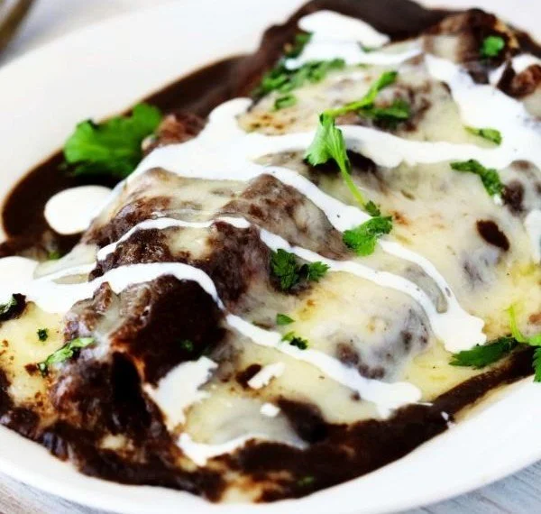 Plate of enfrijoladas topped with black bean sauce and garnishes