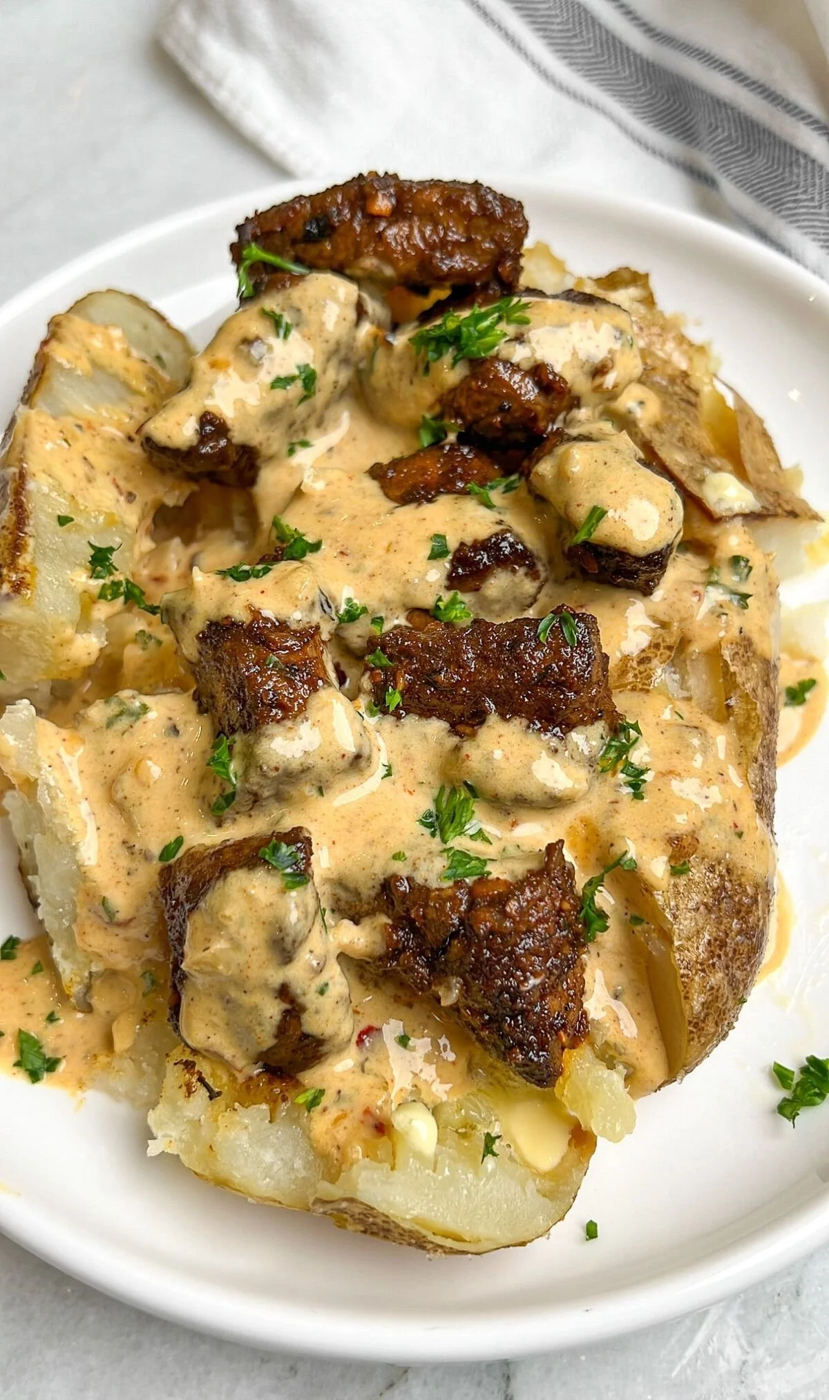Steak bites atop a loaded baked potato, garnished and ready to eat.